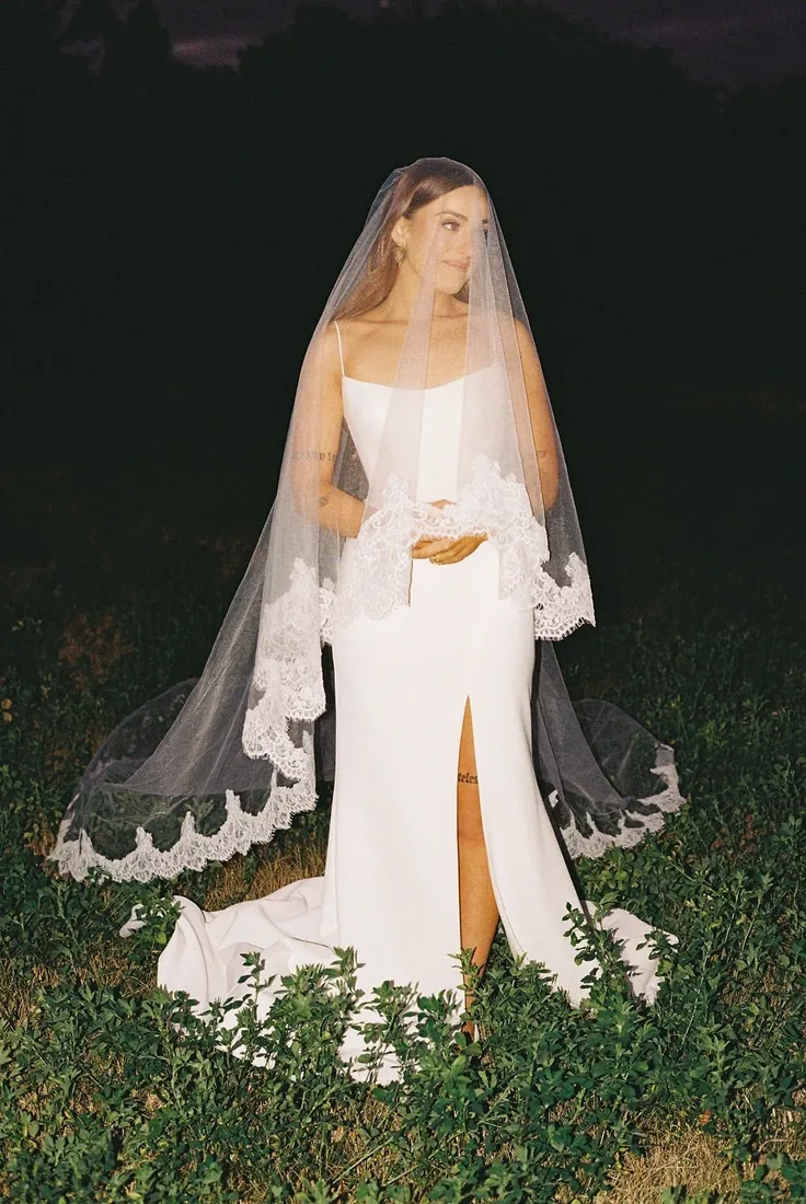 Karly standing in her wedding dress and lace-trimmed veil in the garden at night