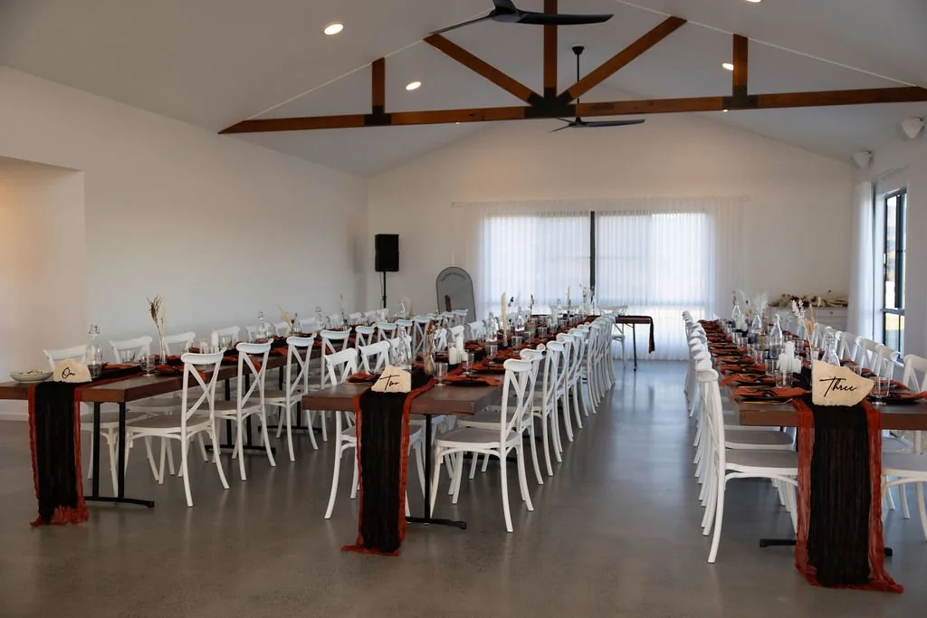 Reception room set with long tables and dark red table runners under the timber beam ceiling