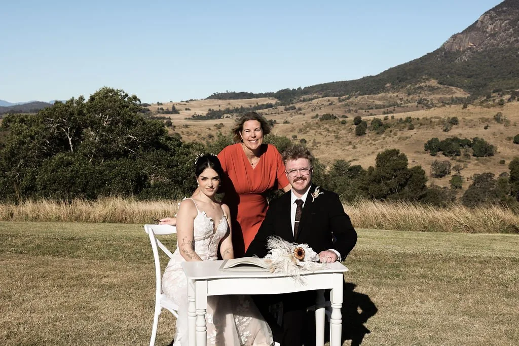 Kate and Jacob signing the register with the celebrant standing behind them, mountains in the background