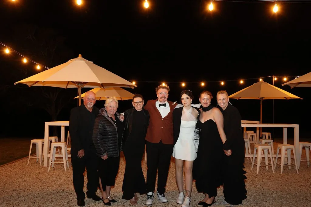 Family and friends gathered together at night under festoon-lit umbrellas