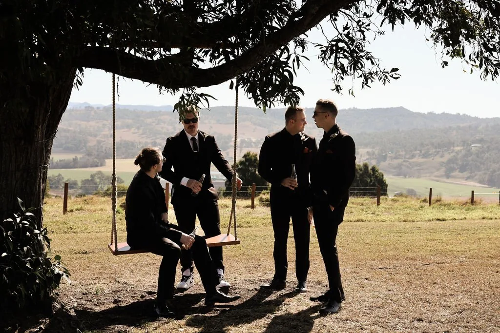 Groomsmen relaxing on a wooden swing under a tree with mountain views