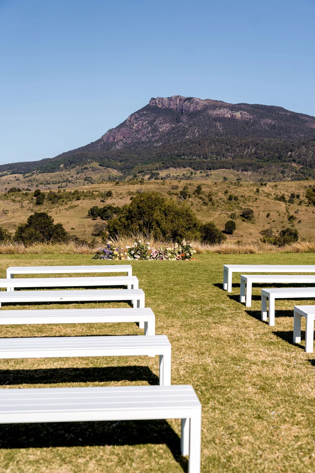 Rows of empty white benches facing a wildflower ceremony arrangement, mountain views behind