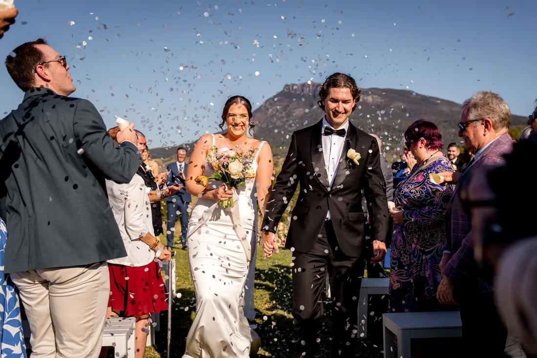 Kylee and Cameron walking back down the aisle through confetti as guests celebrate