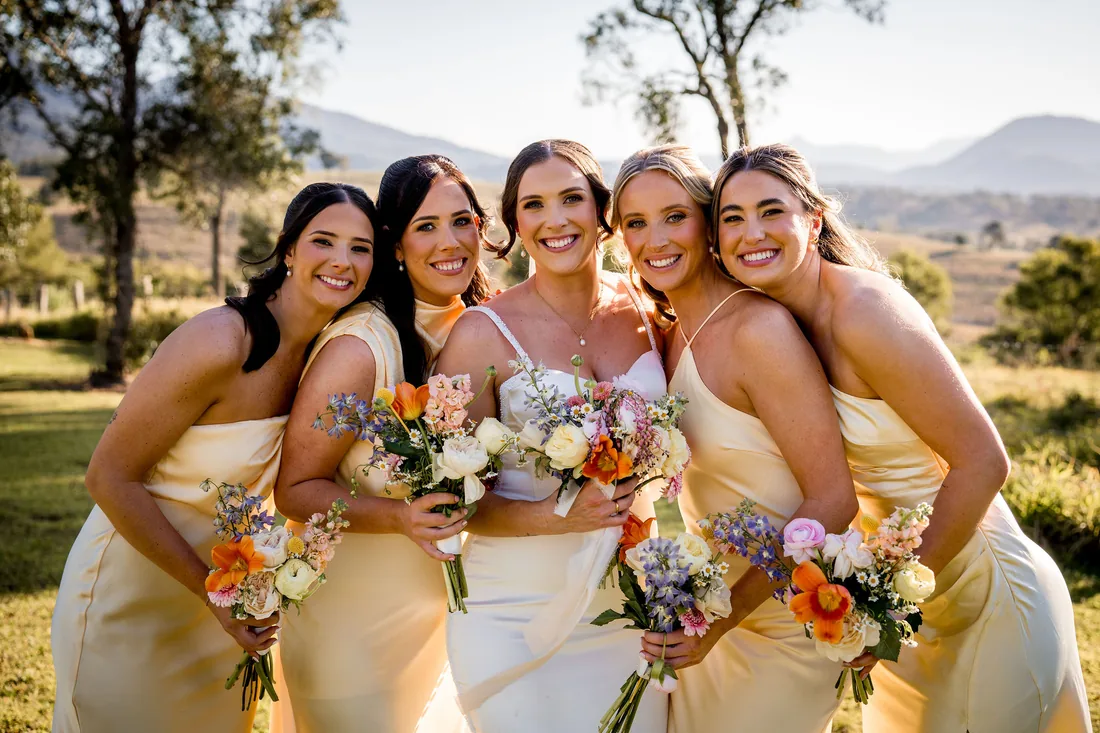 Kylee laughing with her four bridesmaids, each holding colourful wildflower bouquets