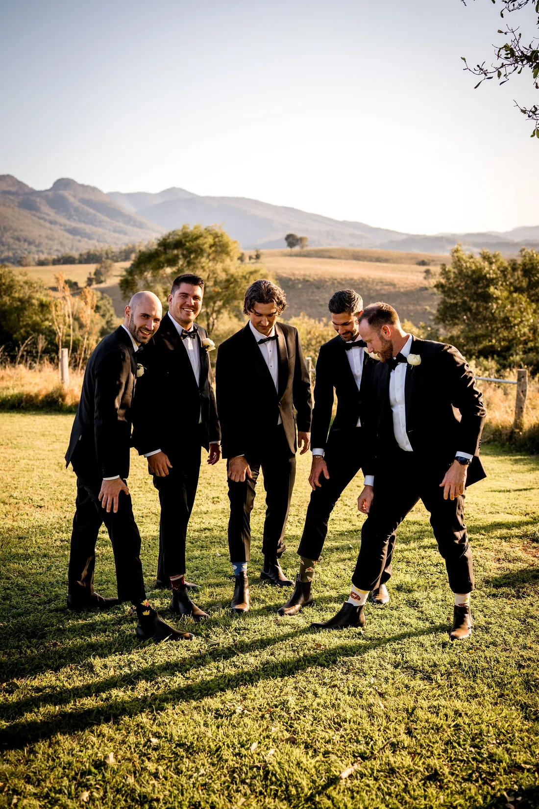 Groomsmen laughing together in a golden paddock at sunset