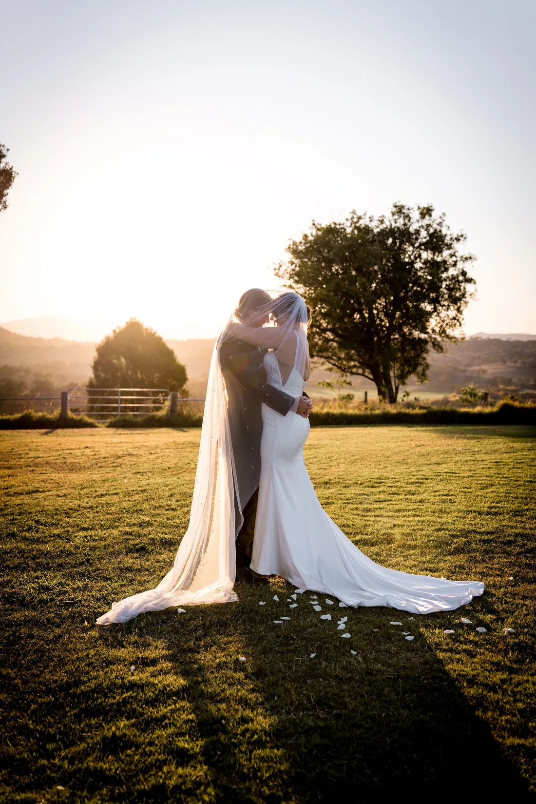Kylee and Cameron kissing under her veil backlit by the setting sun