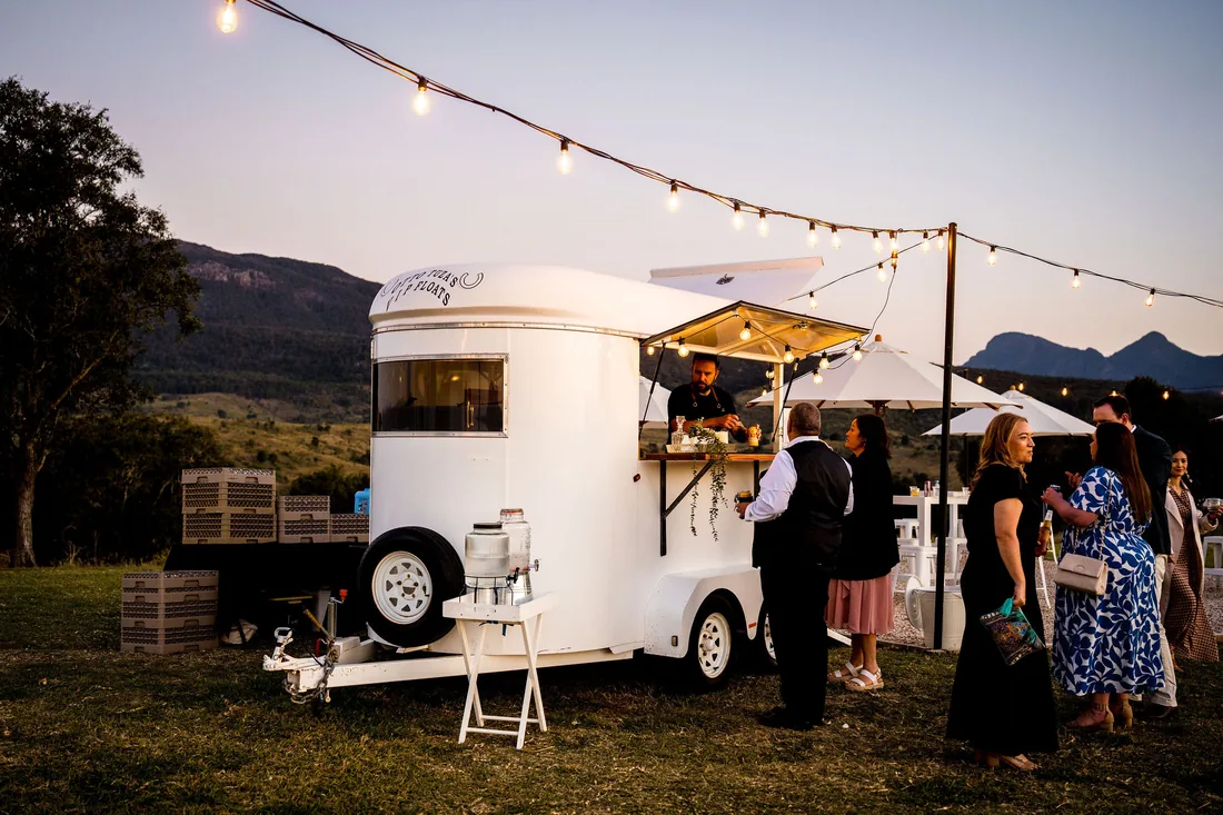 Guests gathering at the mobile bar caravan under string lights at dusk