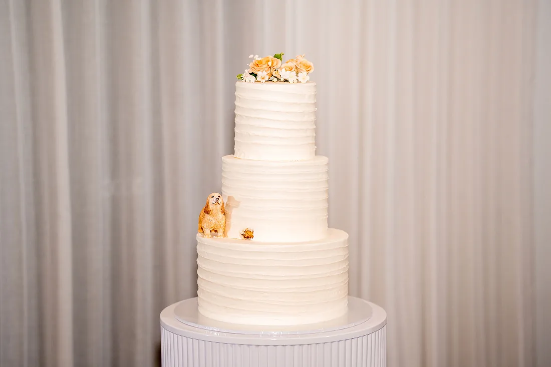 Three-tiered wedding cake topped with fresh flowers and a small dog figurine