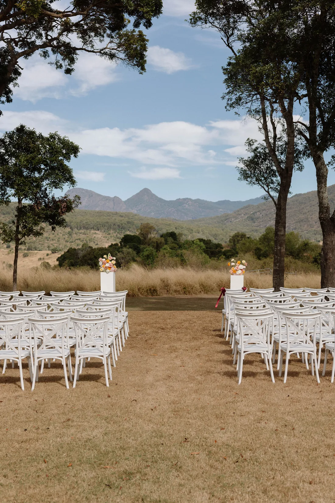Rows of empty ceremony chairs either side of the aisle, floral pillars and mountain views
