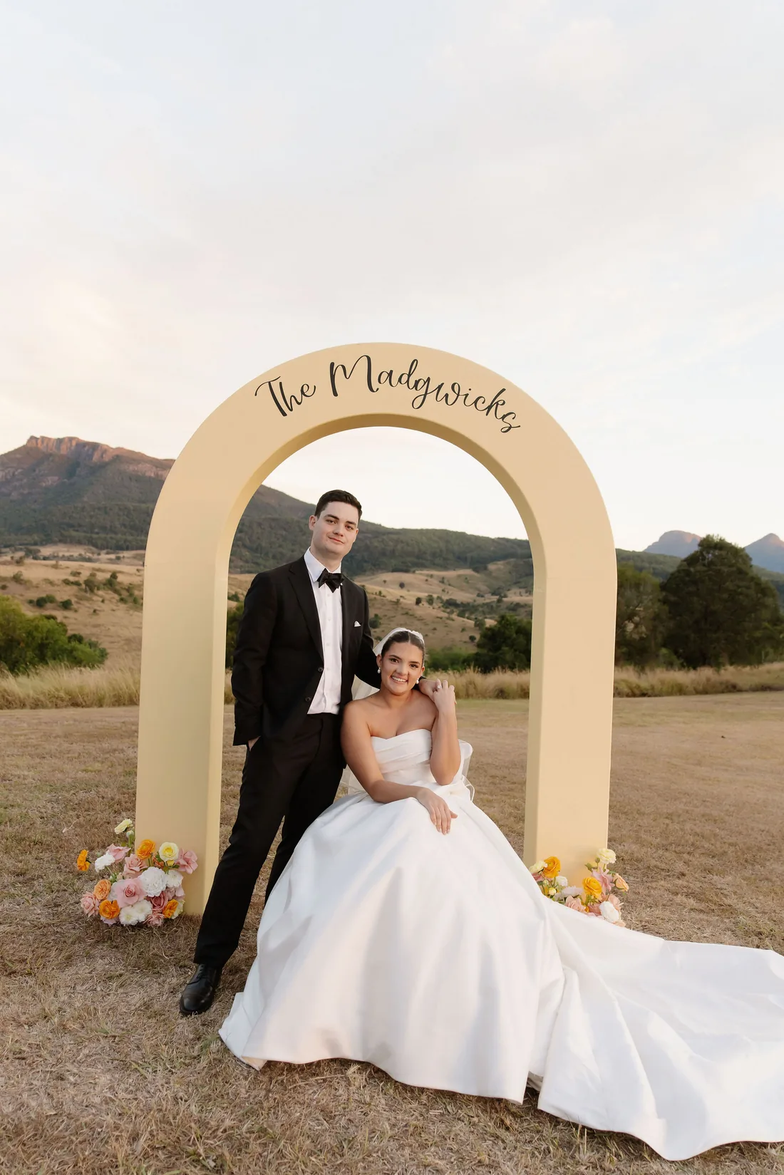 Connor and Laura posing under "The Madgwicks" arch, styled with pink and orange florals