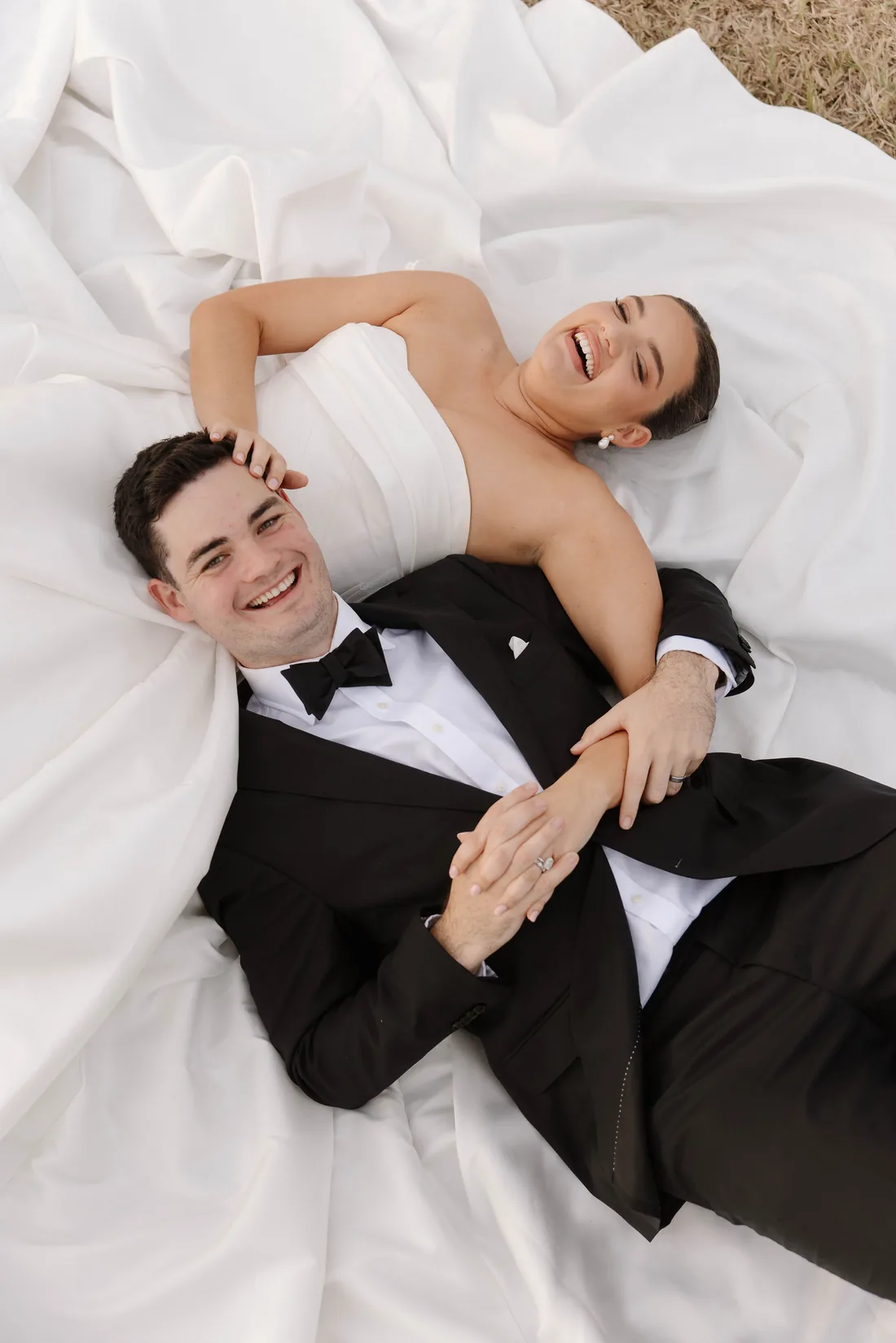 Laura and Connor lying together laughing, her dress spread out around them