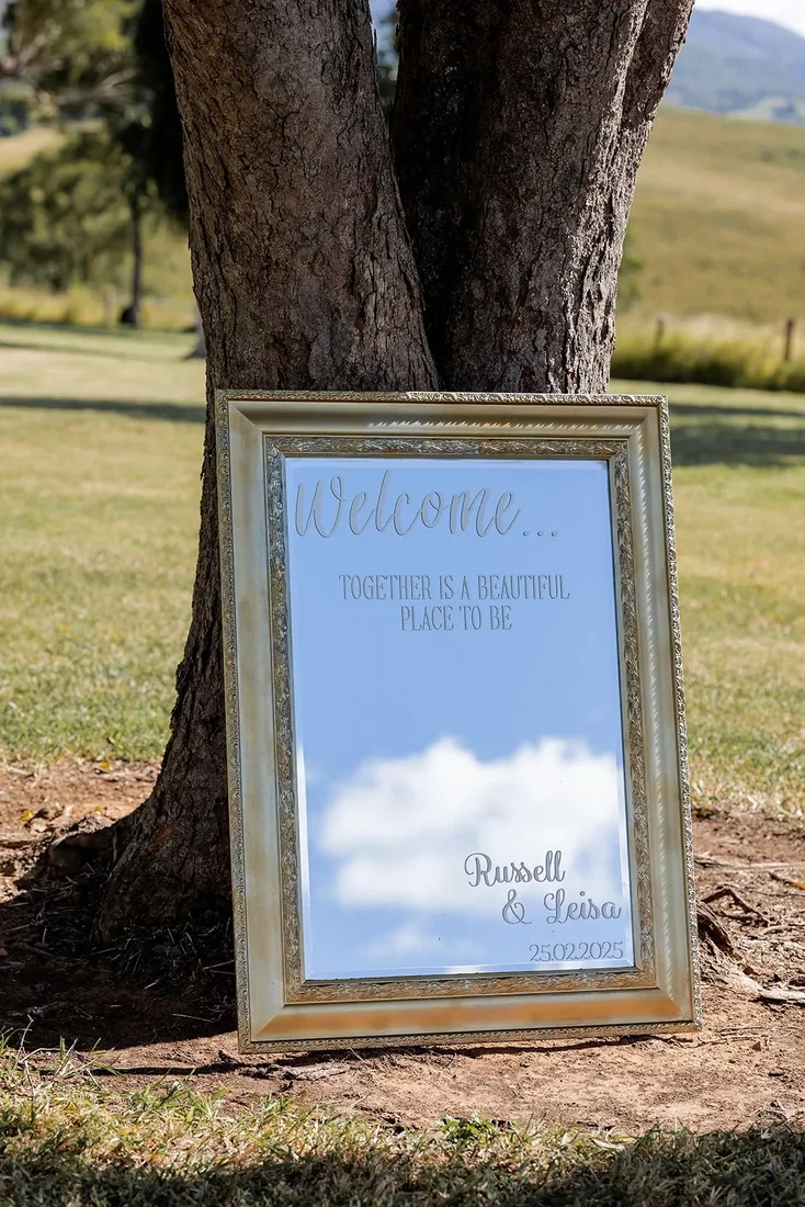 Vintage mirror welcome sign leaning against a tree, reading Russell and Leisa