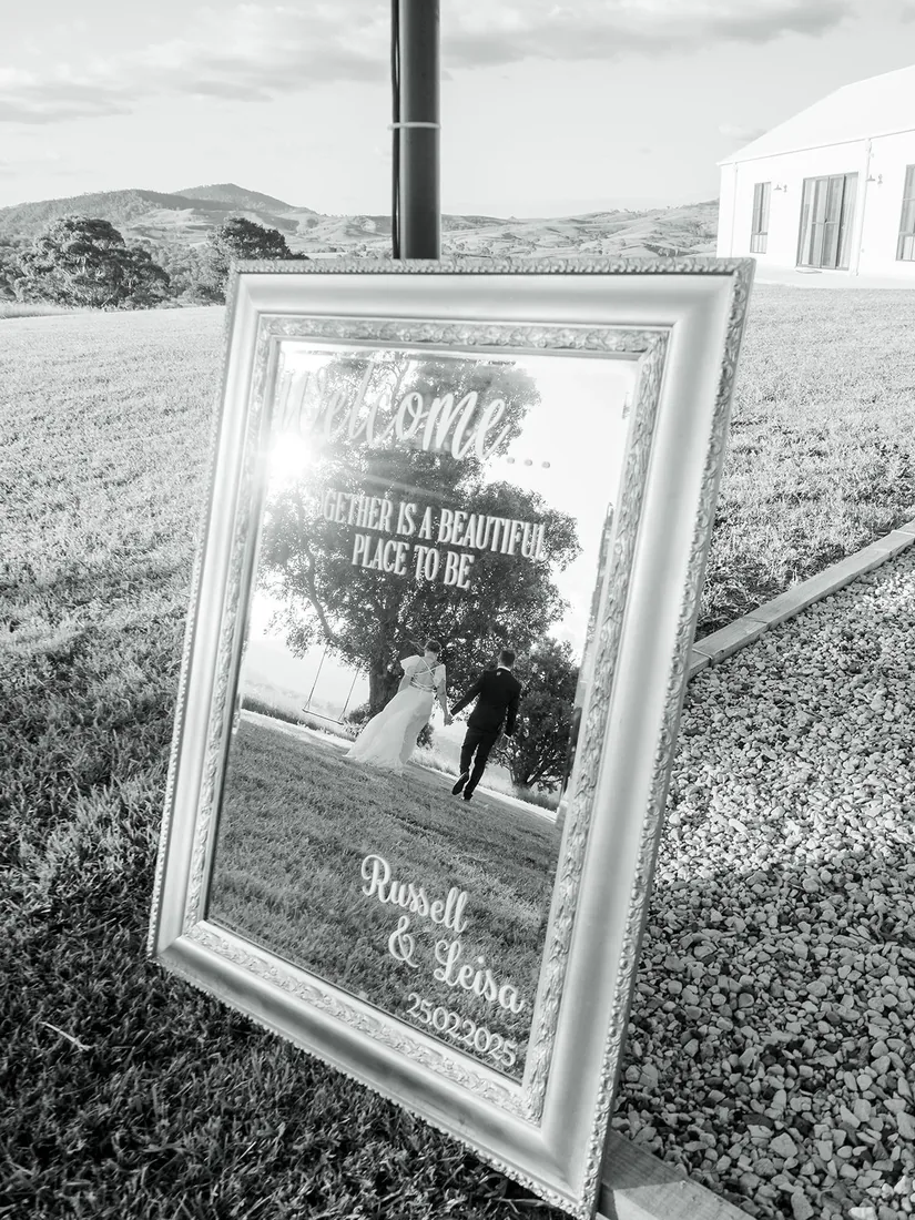 Black and white photo of the vintage mirror welcome sign reflecting the couple walking hand in hand