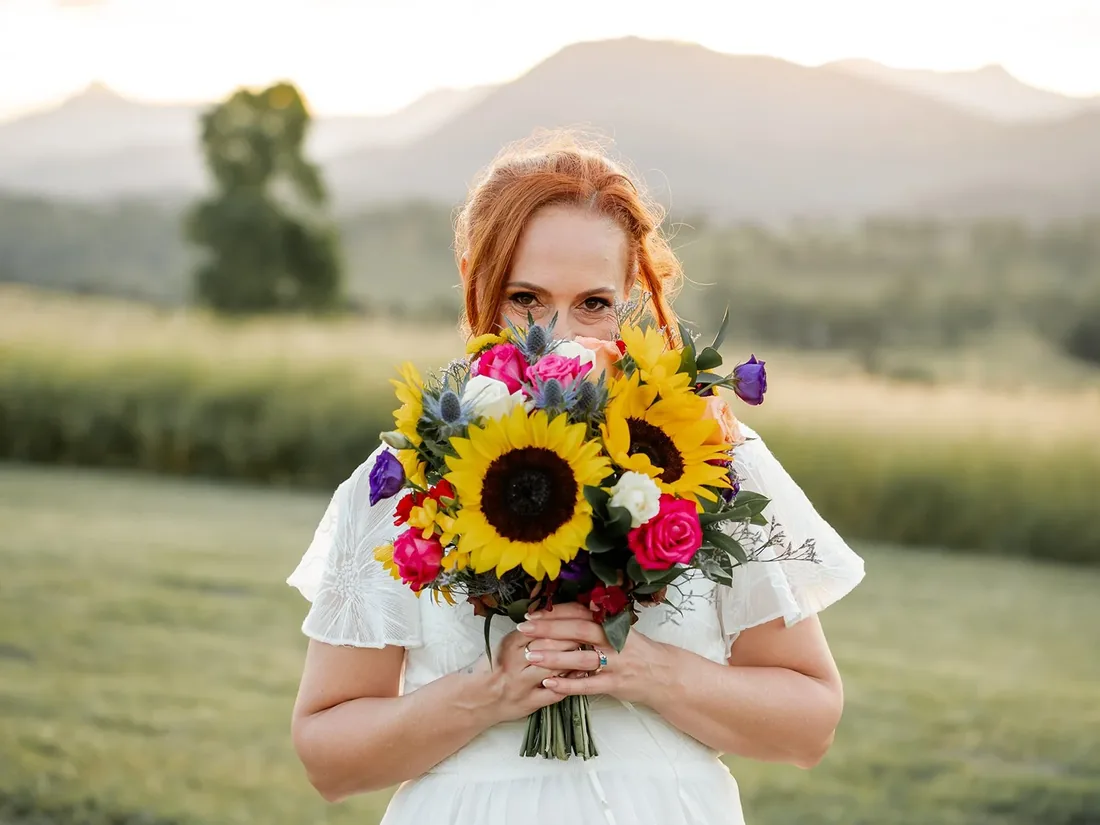 Leisa holding a bouquet of sunflowers and native blooms up in front of her face