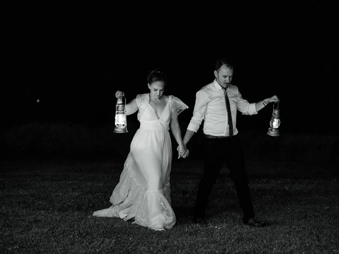 Black and white photo of Leisa and Russell walking hand in hand at night, each holding a lantern