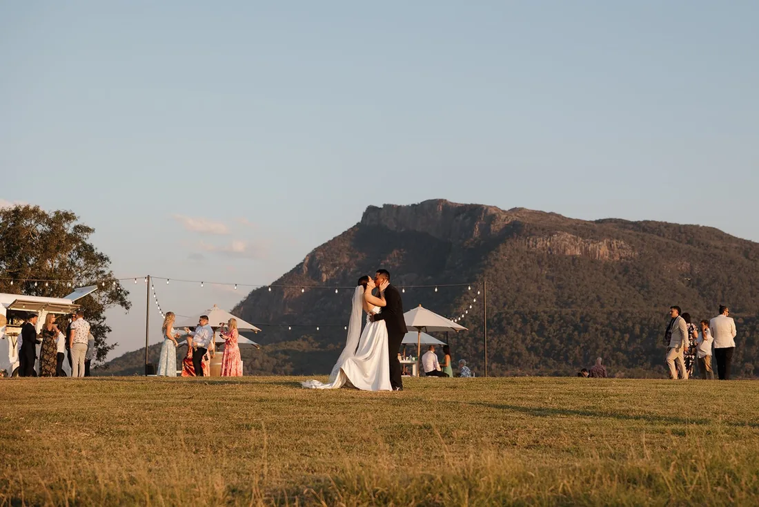 Megan and Lyall kissing at golden hour under festoon lighting with mountains behind them