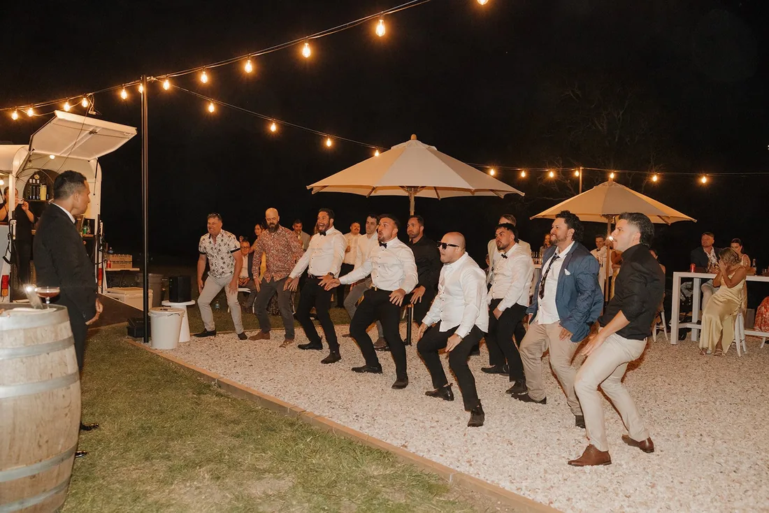 Groomsmen performing a haka under festoon lighting at night