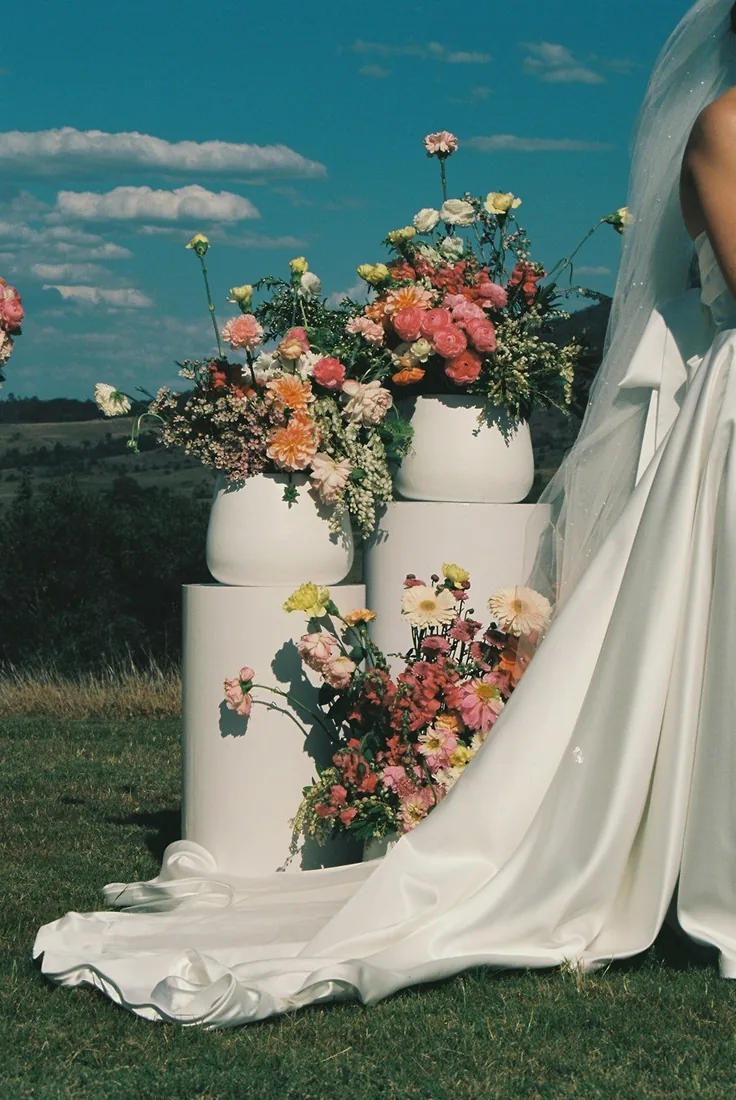 Floral arrangements on white pedestals beside the bride's dress train