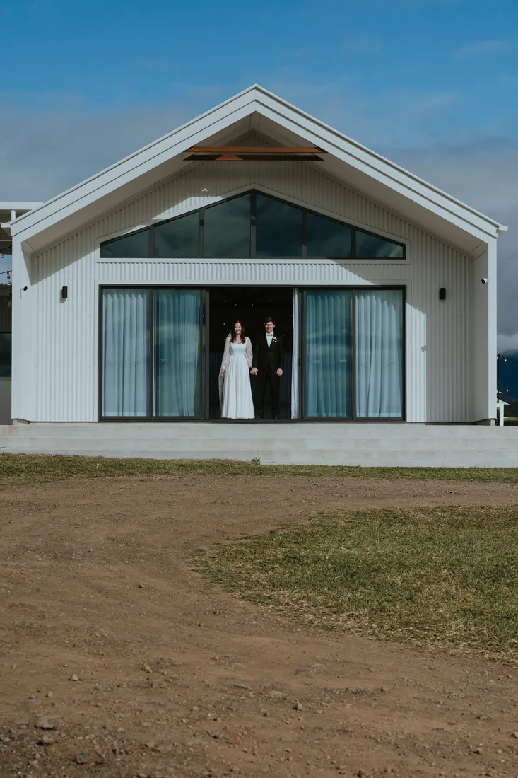 Melanie and Nathan standing together in the open doorway of the white reception venue