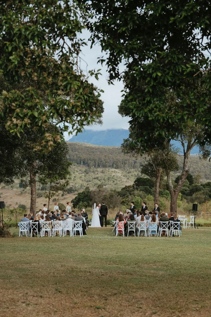 Guests seated for the ceremony beneath large shade trees with mountain views