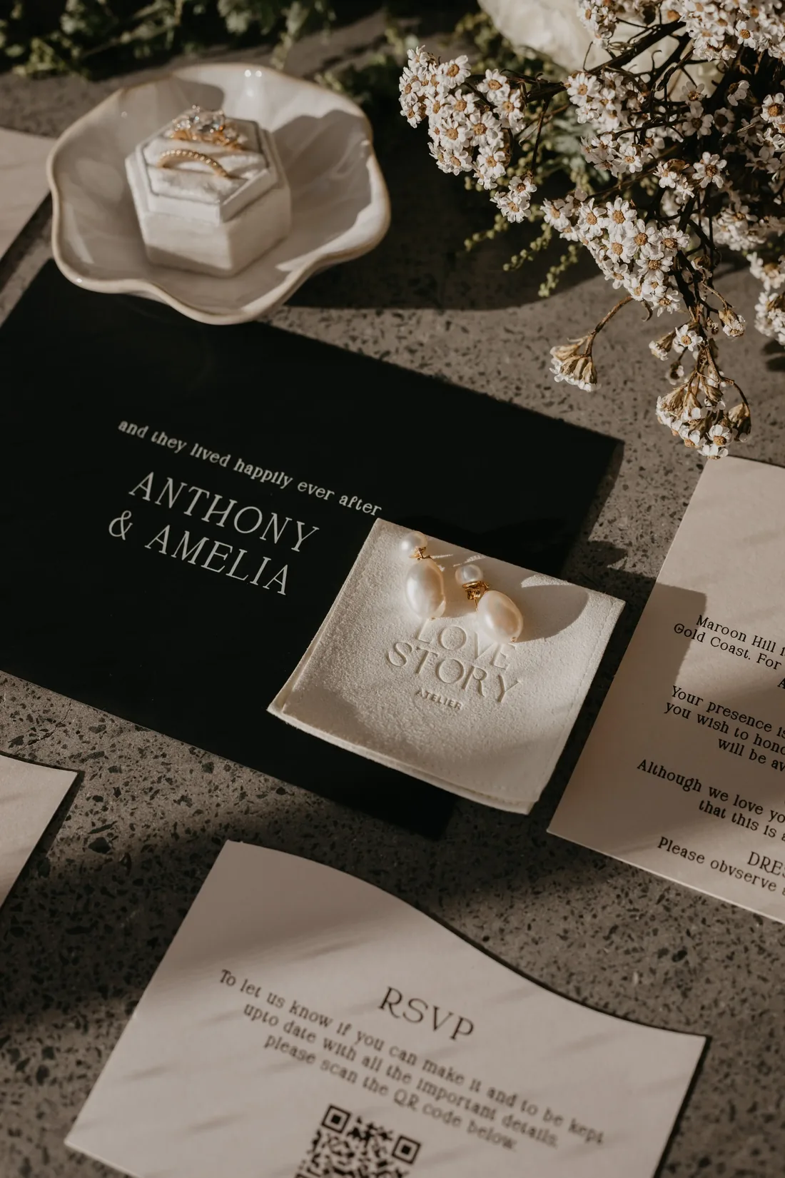 Black invitation suite for Anthony and Amelia styled with pearl drop earrings, a ring box and native florals