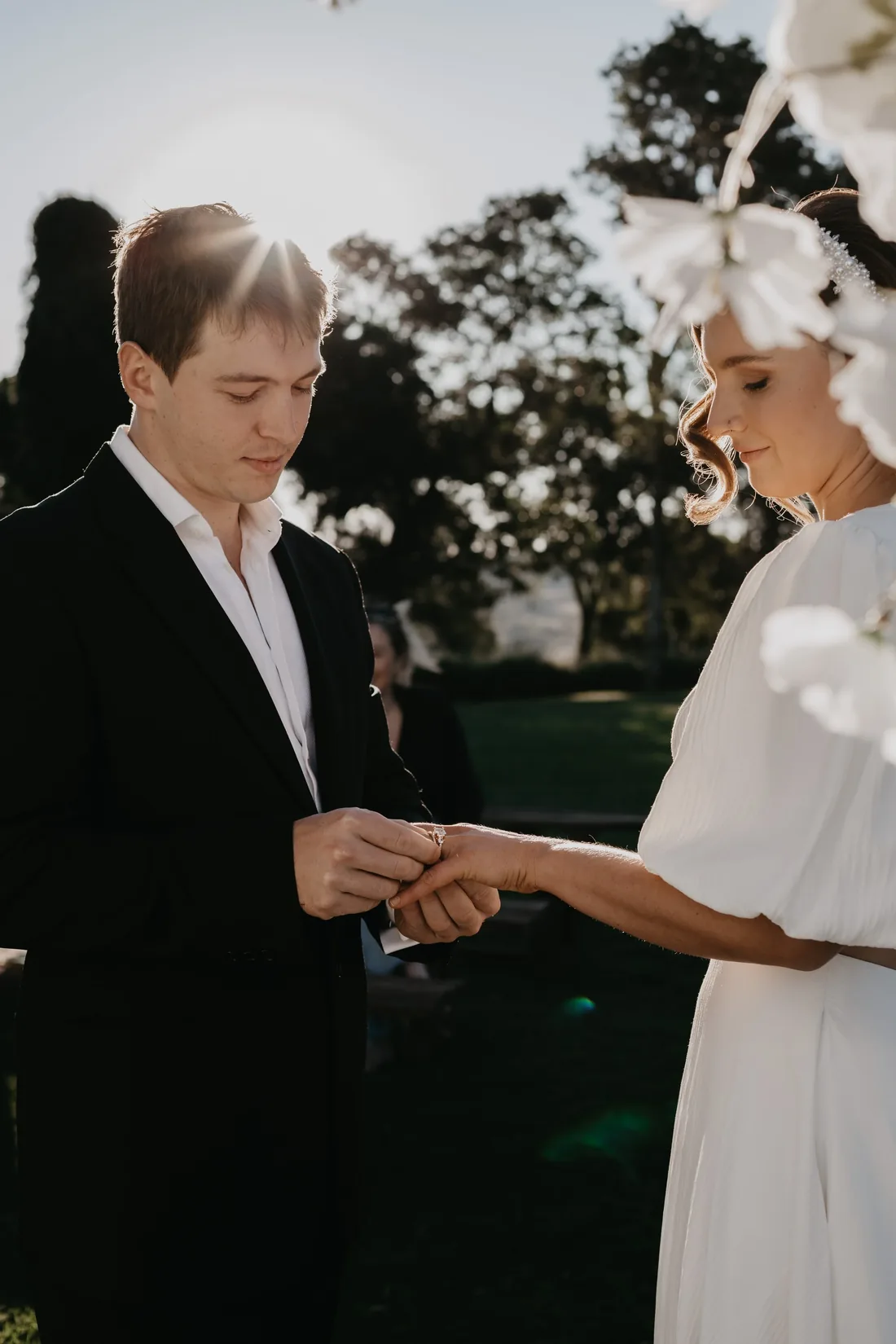 Groom placing a ring on the bride's finger during their vows, golden backlight