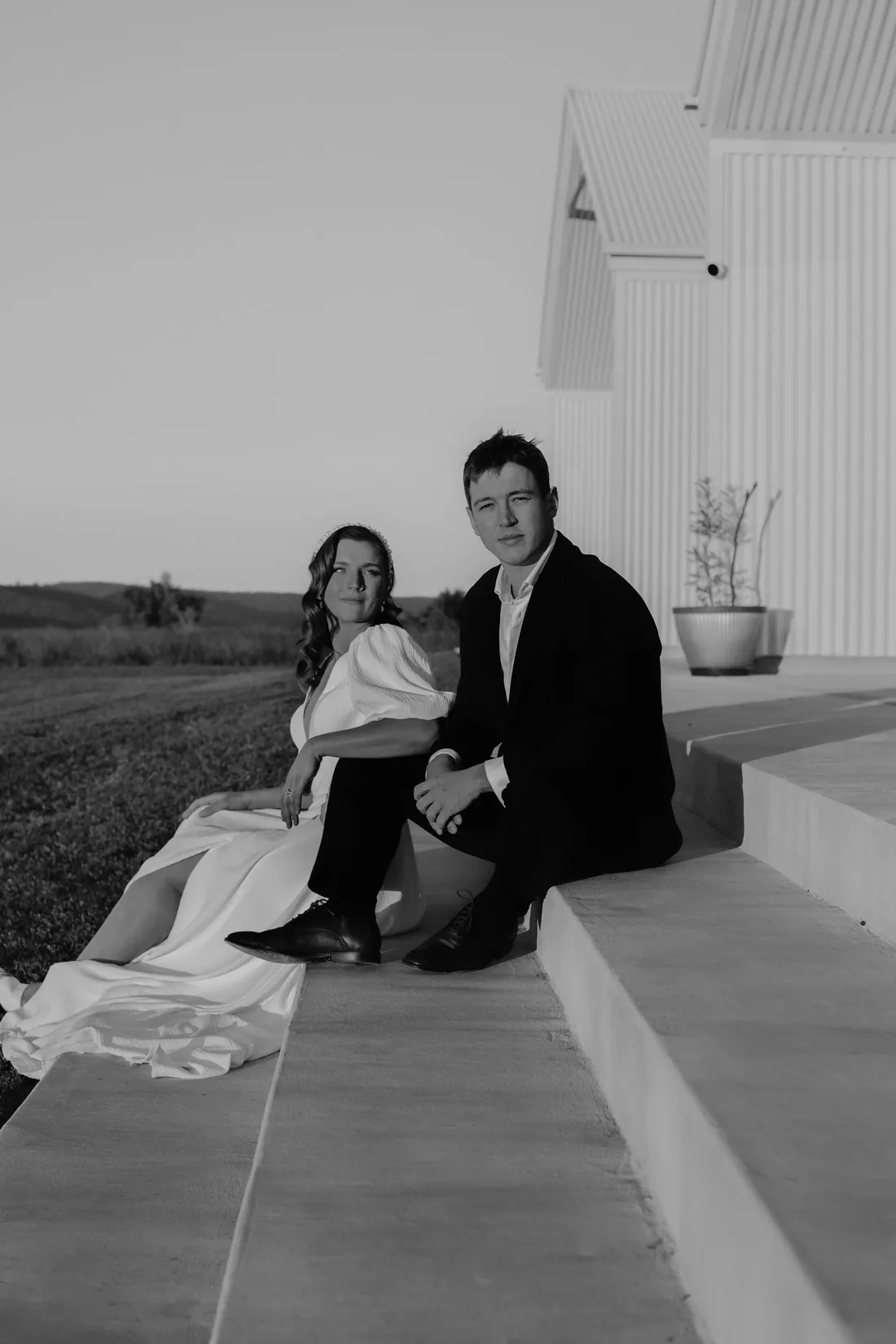 Black and white portrait of the couple sitting together on the venue steps at dusk