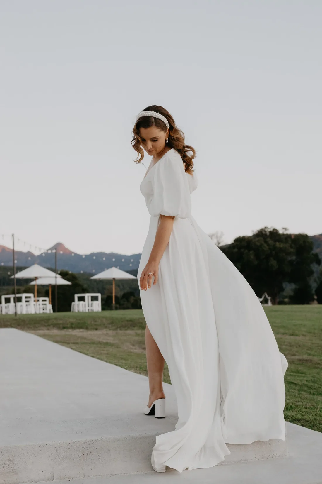 Bride in a flowing white gown with a beaded headband, standing on the steps at golden hour