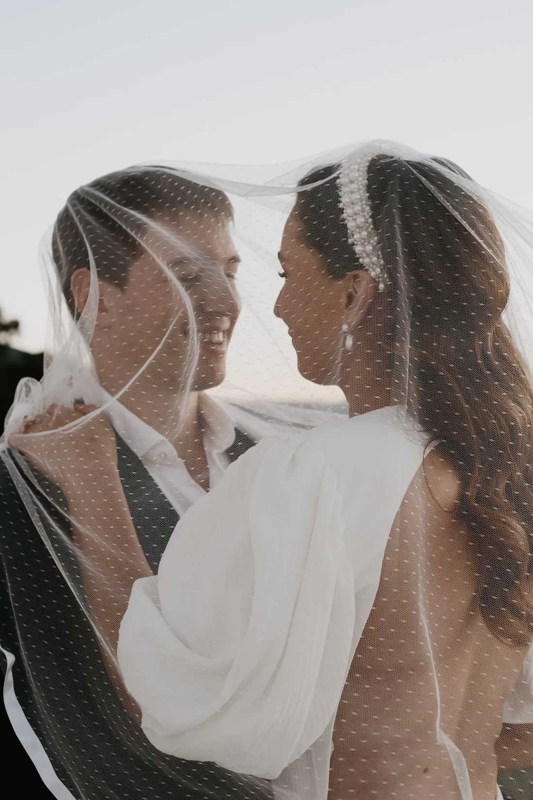 Bride and groom sharing a moment together under a dotted veil in golden hour light