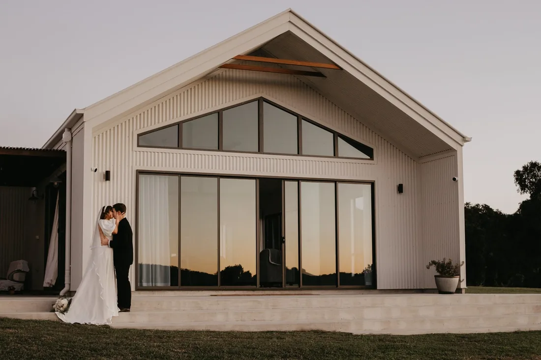 Bride and groom kissing in front of the reception venue's glass doors at dusk
