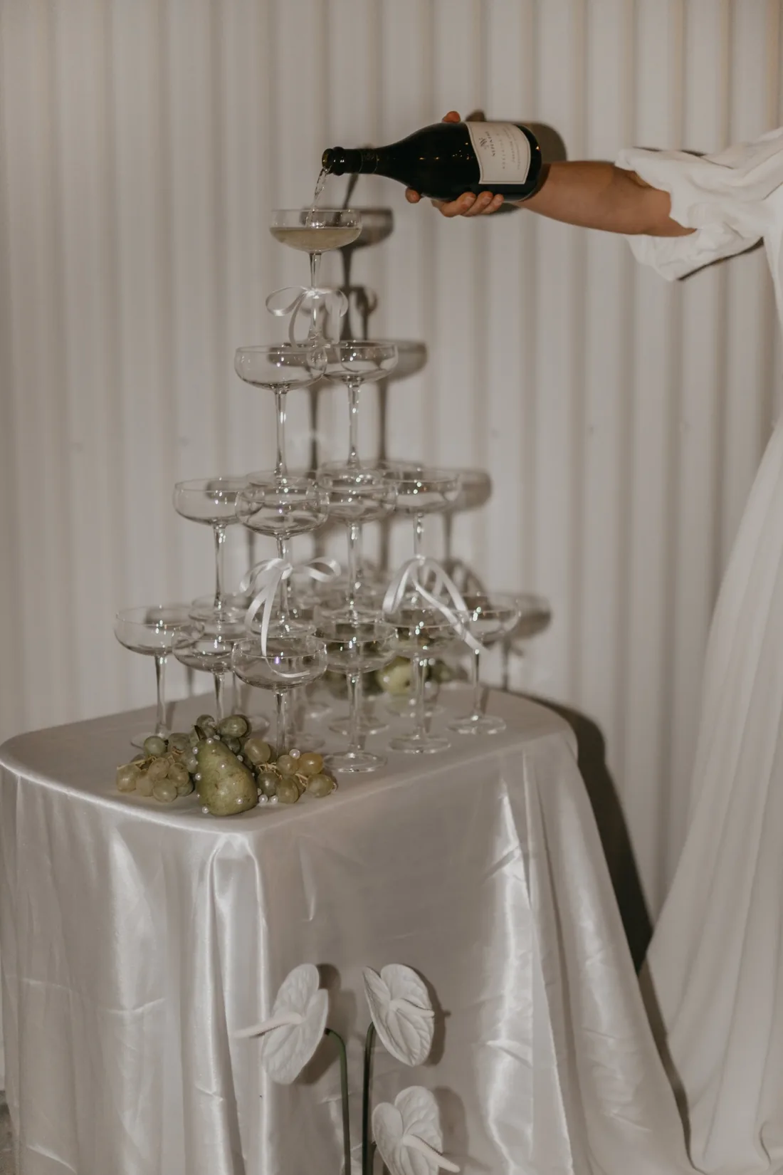 Champagne being poured into a tower of coupe glasses styled with fresh pears