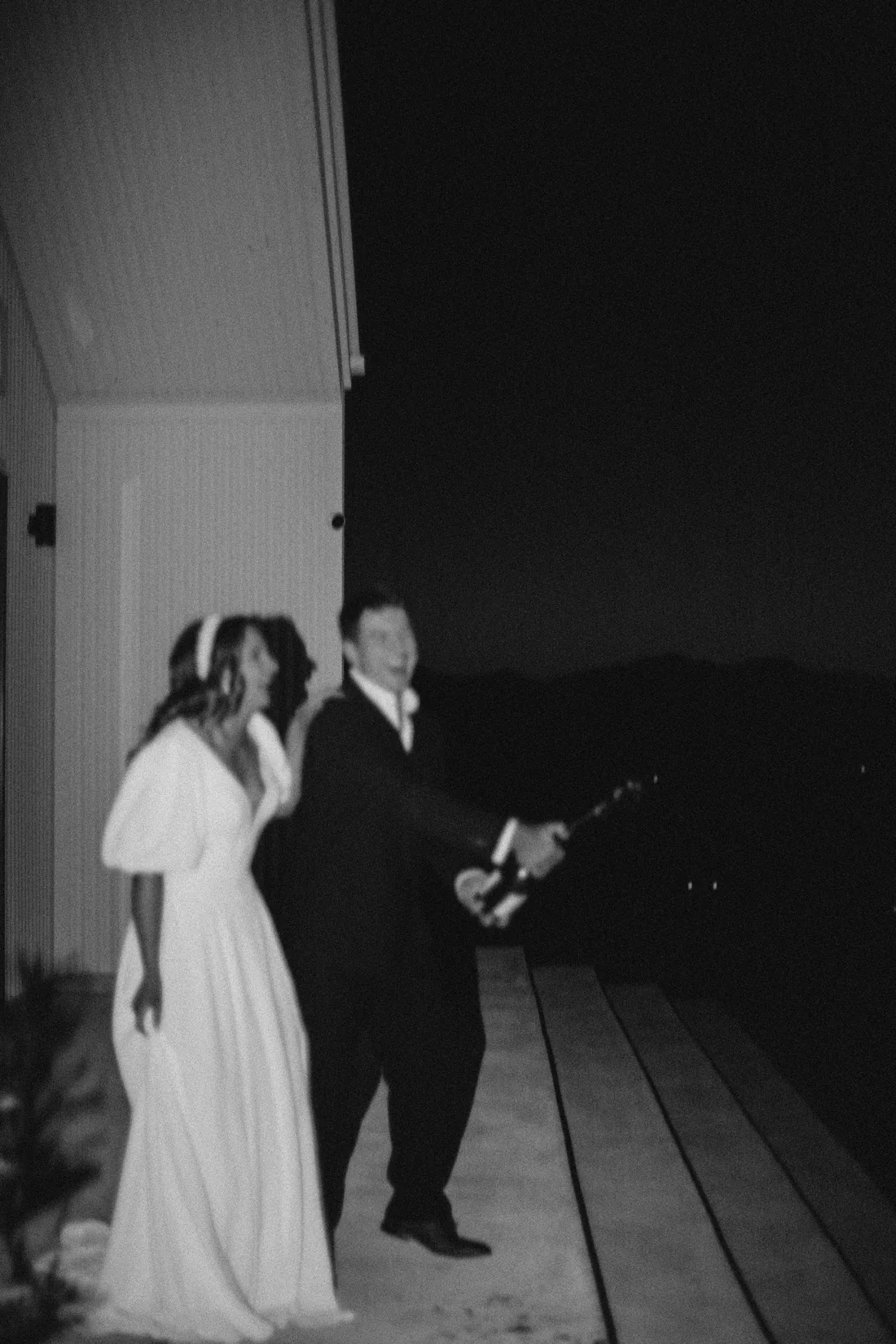 Black and white night photo of the bride and groom laughing on the venue deck
