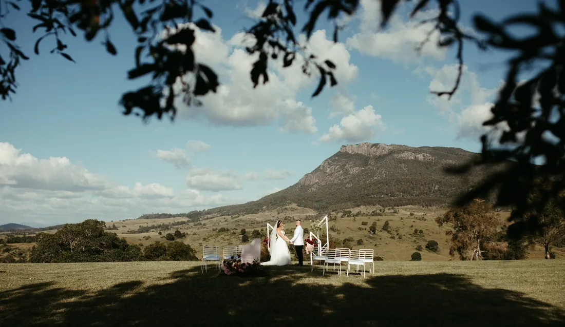 Ceremony styled beneath a large tree with mountain views, celebrant and couple at the altar