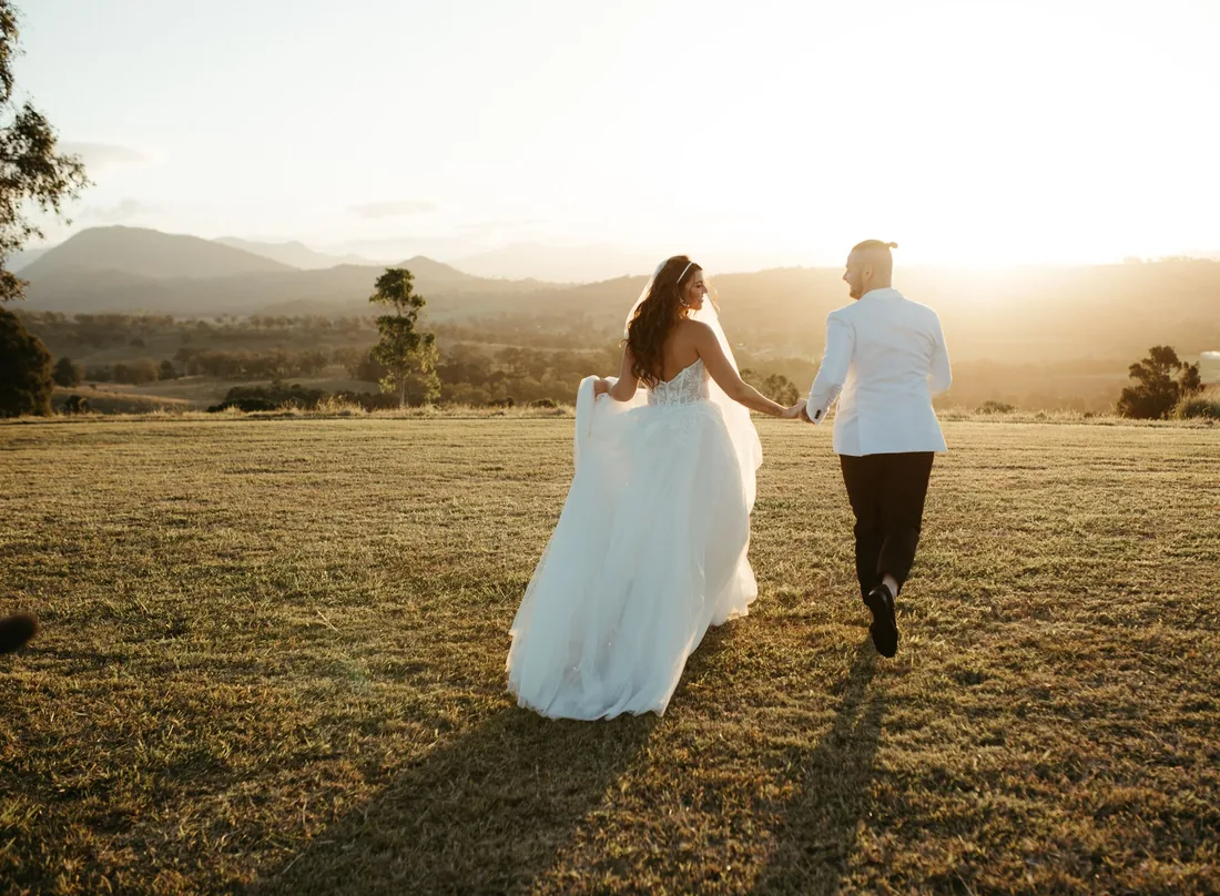 Bride and groom walking hand in hand across the paddock at golden hour