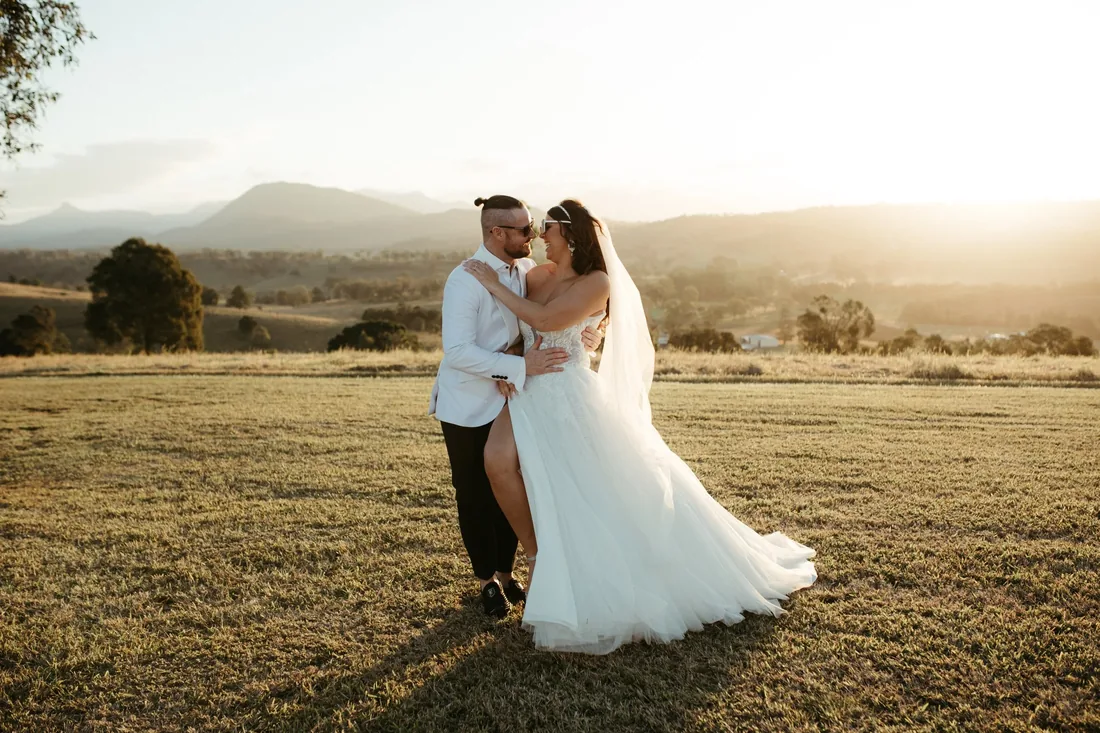 Groom nuzzling the bride's cheek in a golden field at sunset