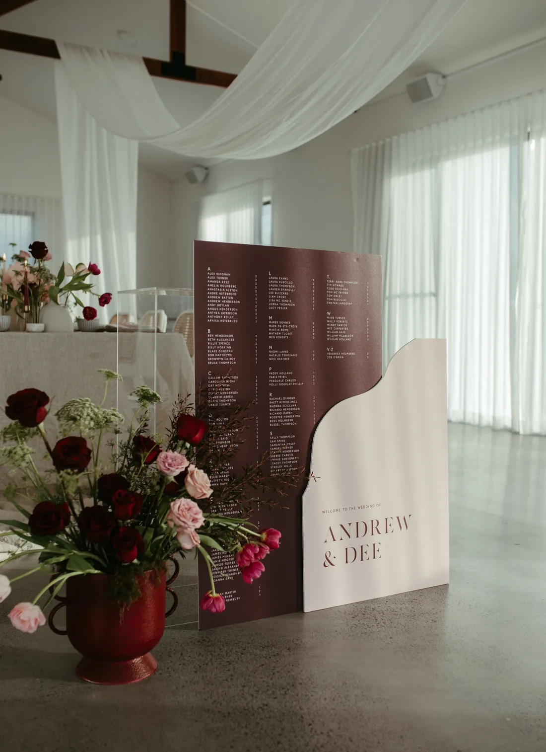 Seating chart styled in burgundy and blush tones beside a floral arrangement, reading Andrew and Dee