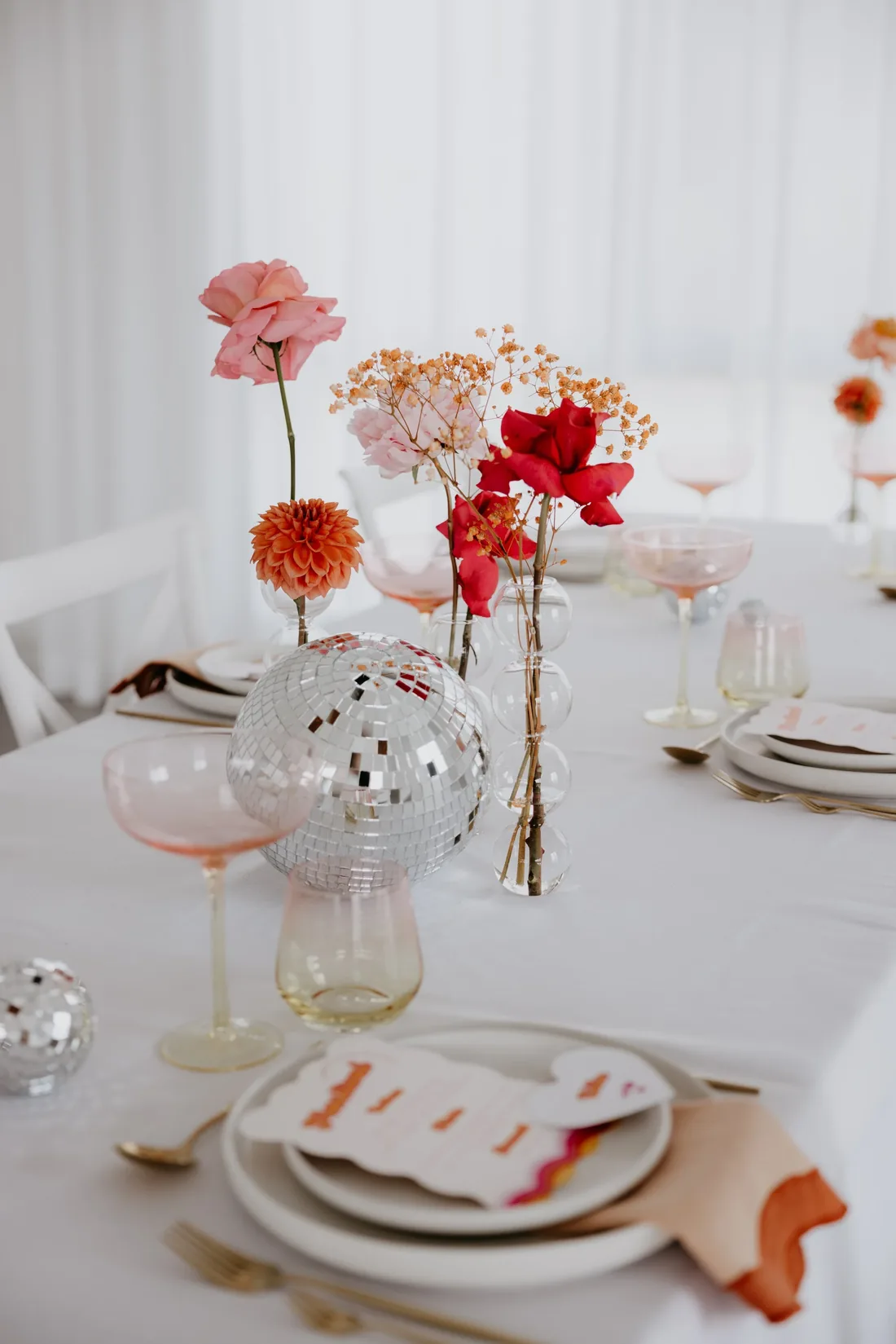 Table setting with disco balls, pink and orange florals, and a numbered place card in a retro font