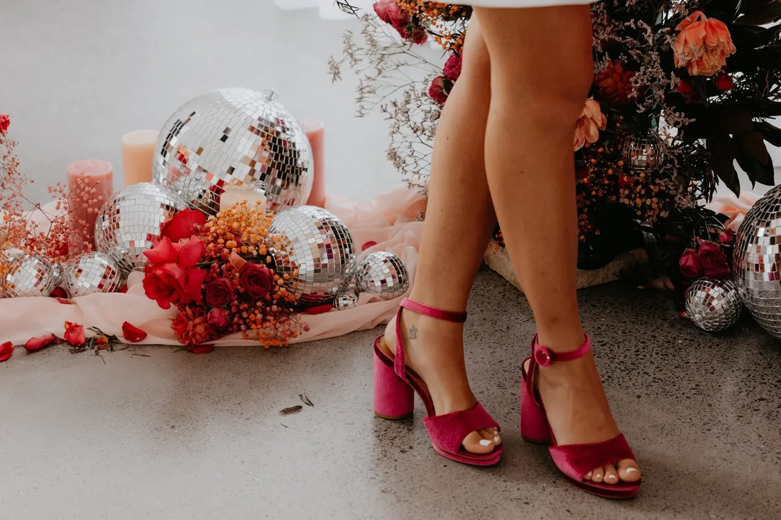 Close-up of hot pink block-heel sandals styled beside disco balls and red roses