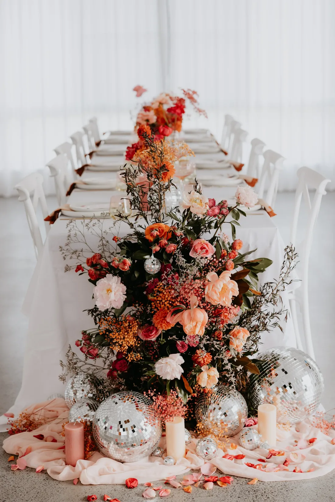 Long reception table styled with a lush floral and disco ball runner in red, orange and pink tones