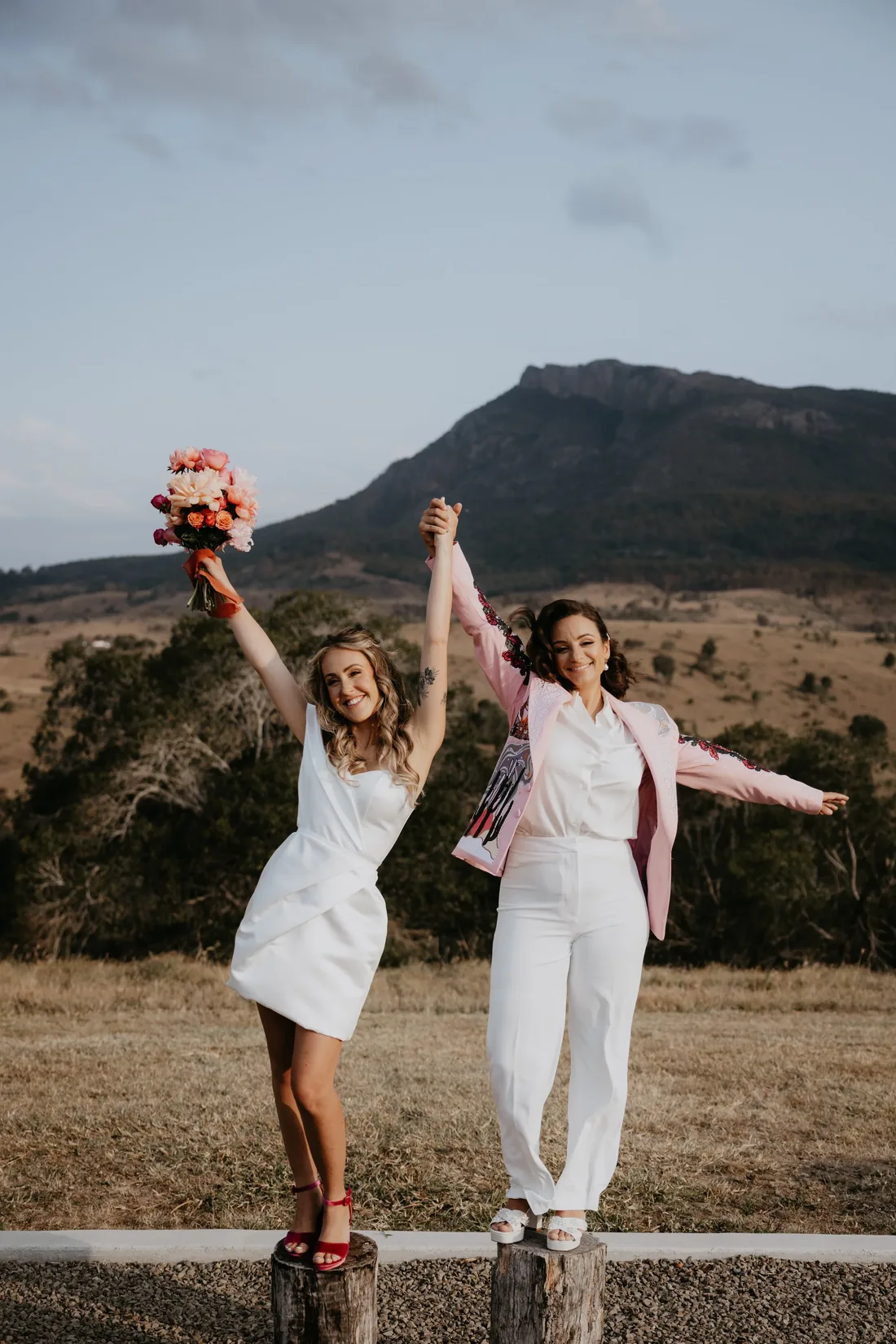 Two brides celebrating with arms raised in a golden paddock at Maroon Hill Estate