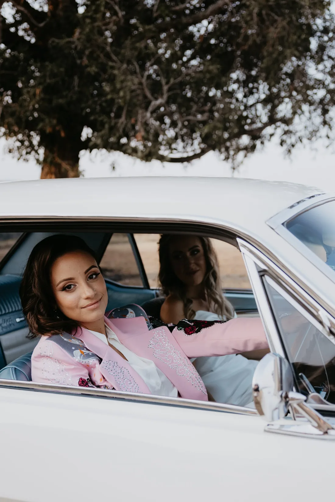 Two brides sitting together in the back seat of a vintage convertible