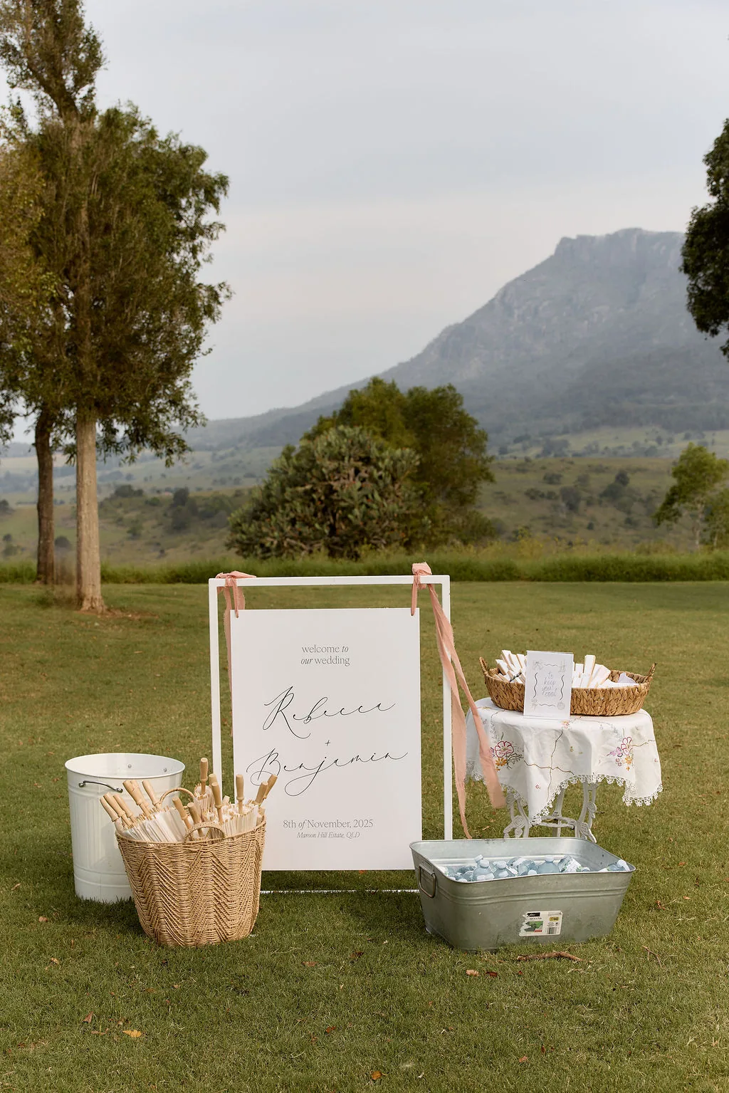 Rebecca and Benjamin wedding welcome sign styled with ribbon and parasols, mountain backdrop