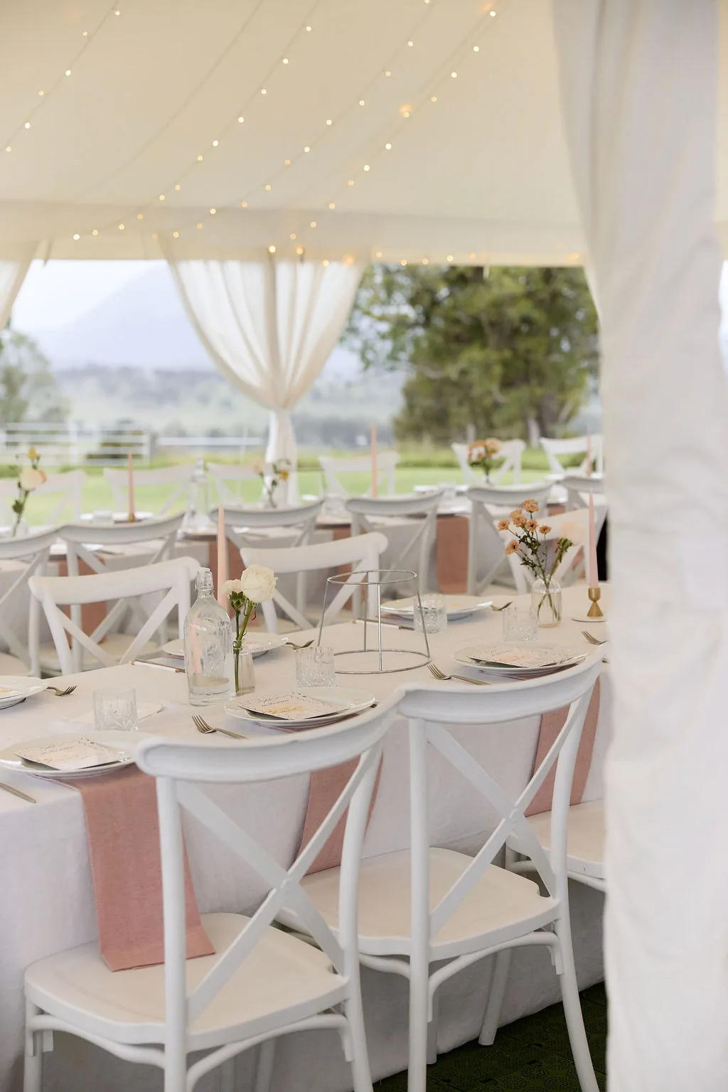 Reception marquee table setting with blush linen runners and fairy lights overhead