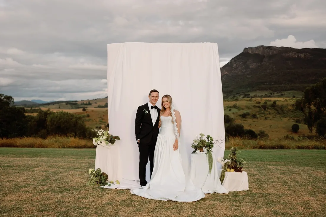 Samara and Ryan in front of a styled white ceremony backdrop at Maroon Hill Estate