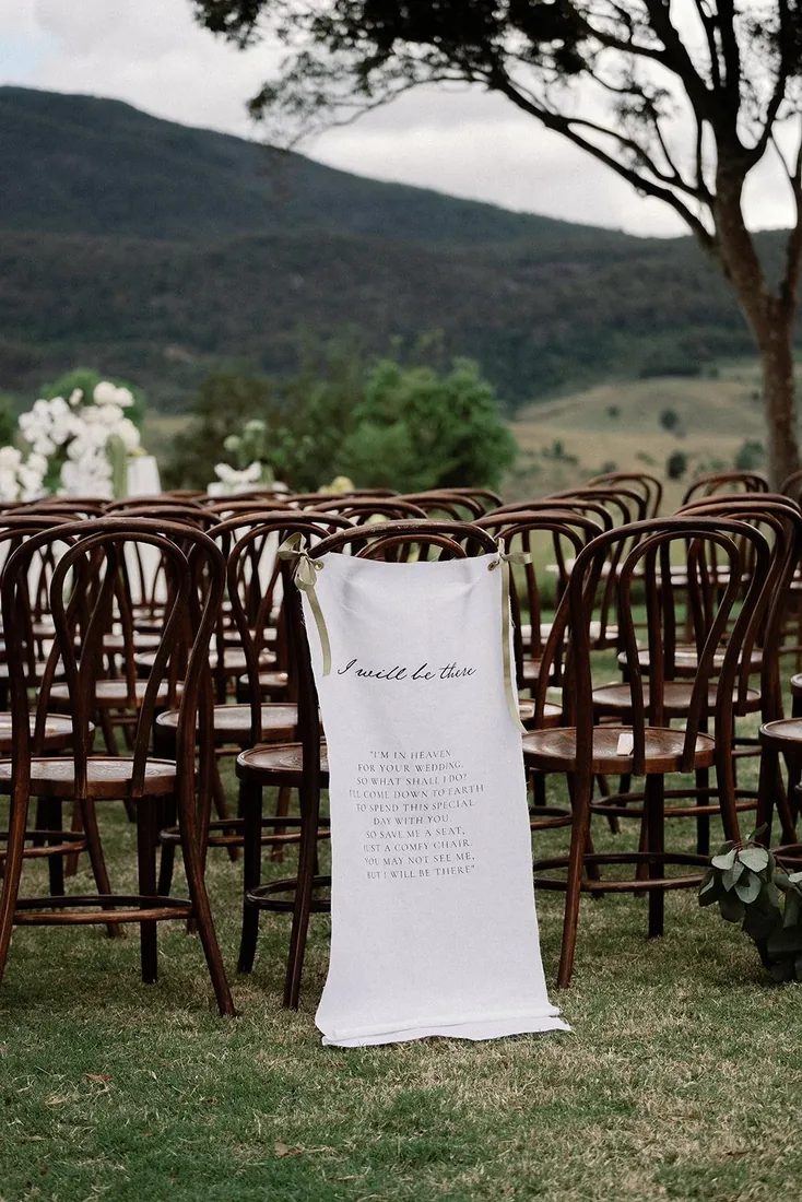 Ceremony seating with bentwood chairs, one draped with a ribbon reading I will be there