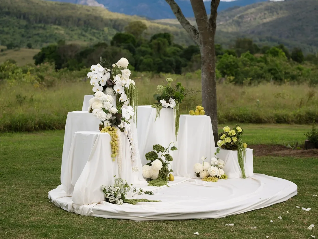White ceremony arbour styled with florals, fruit and pillar stands, mountains behind