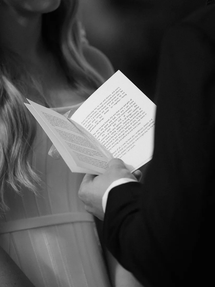 Black and white close-up of the celebrant's notes held between the bride and groom during their vows
