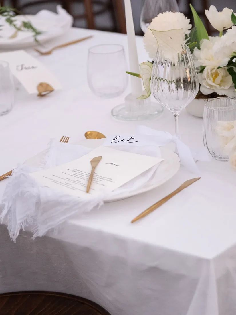 Place setting with gold cutlery, a name card and white floral centerpiece