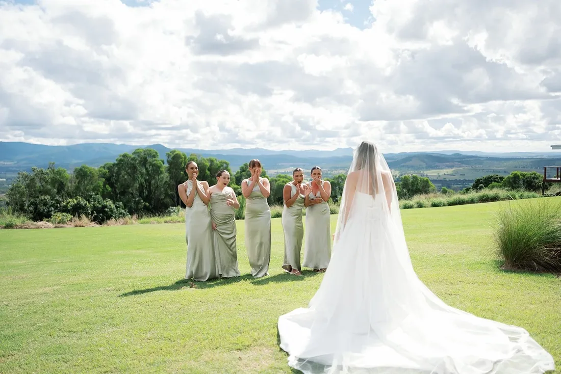 Bridesmaids in sage green gowns applauding as Samara stands with her back to camera, mountain views beyond