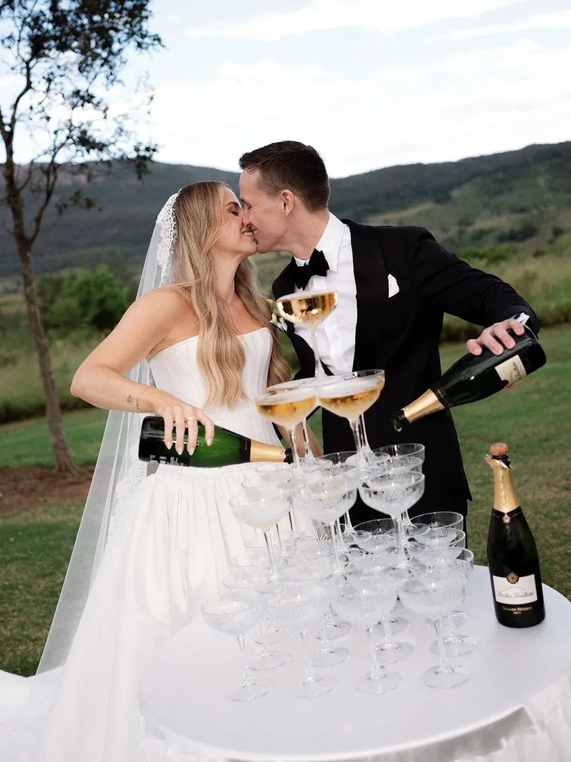 Samara and Ryan kissing while pouring champagne into a tower of glasses